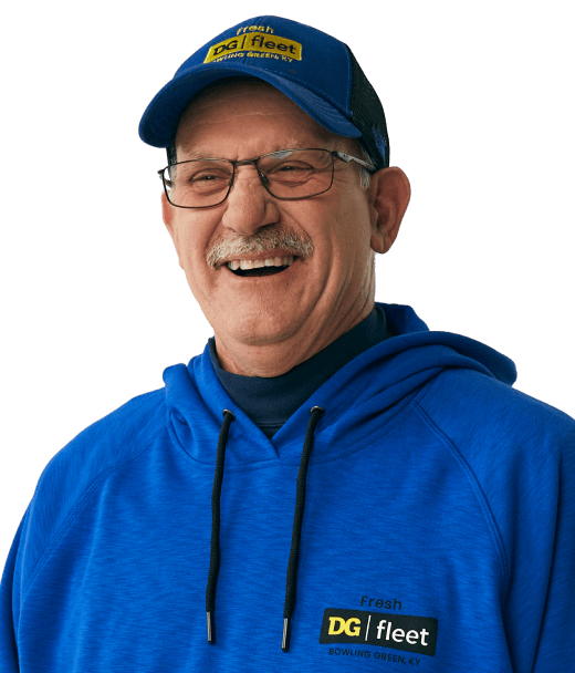 Smiling older man wearing glasses, a blue “DG fleet” cap, and a matching blue hoodie with “DG fleet” logo, standing against a plain light background.