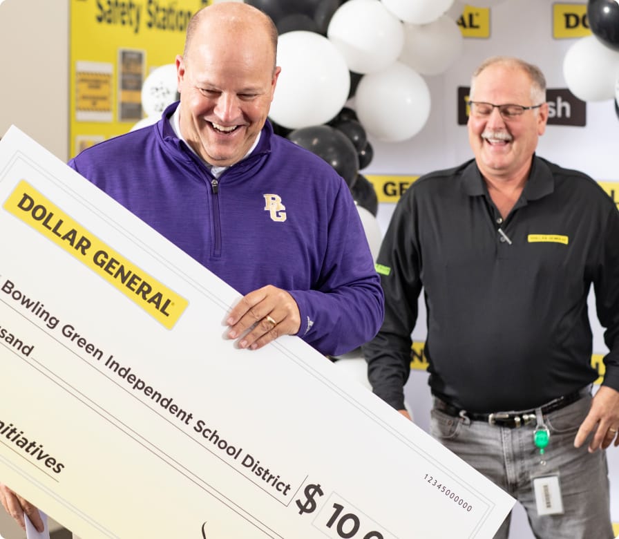 Two smiling men hold an oversized check from Dollar General, made out to Bowling Green Independent School District for $10,000, surrounded by black, white, and yellow balloons.