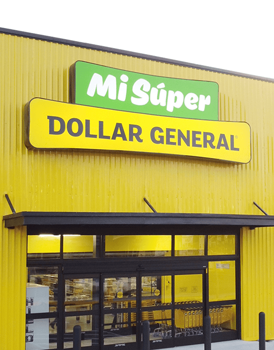 Front entrance of a Dollar General store with a green “Mi Súper” sign above the yellow “Dollar General” sign on a yellow building exterior.